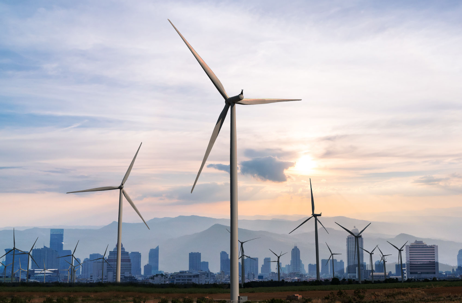 A stock photo of a wind turbine farm with mountains and the sun setting in the background