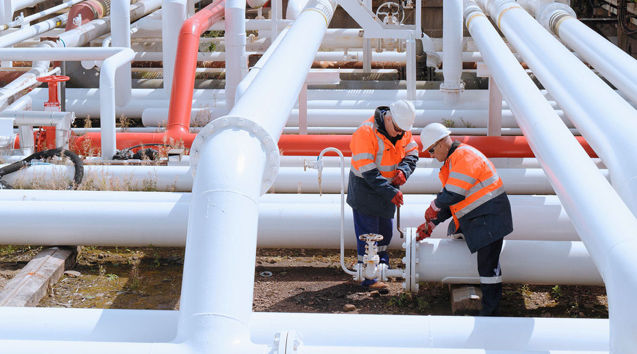 A stock photo of two technicians tightening bolts on a natural gas pipe