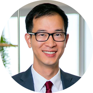 Headshot of an Asian man in a suit smiling, wearing glasses.